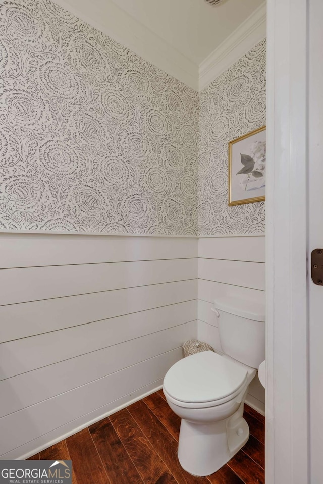 bathroom with toilet, wallpapered walls, crown molding, and wood finished floors