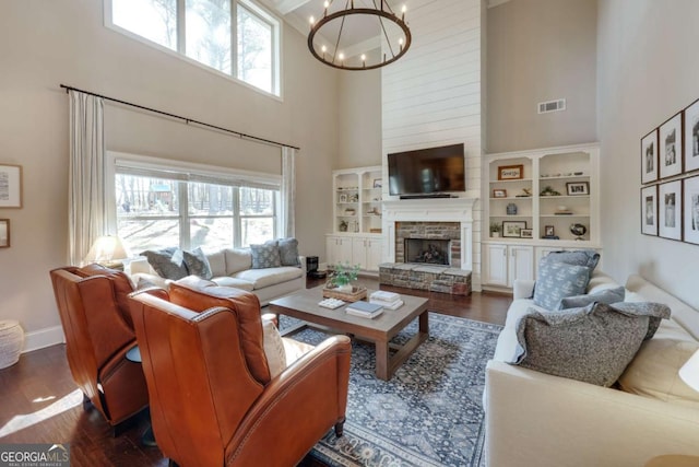 living room featuring a wealth of natural light, dark wood-type flooring, a notable chandelier, and a stone fireplace