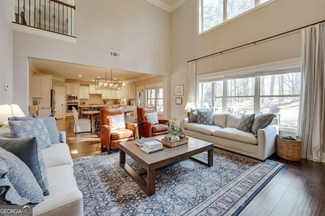 living area featuring an inviting chandelier, visible vents, wood finished floors, and ornamental molding