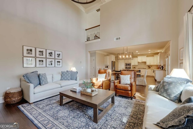 living room featuring a high ceiling, visible vents, a chandelier, and wood finished floors