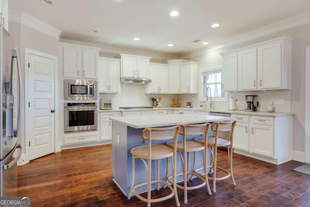 kitchen with under cabinet range hood, stainless steel appliances, a kitchen island, white cabinetry, and light countertops