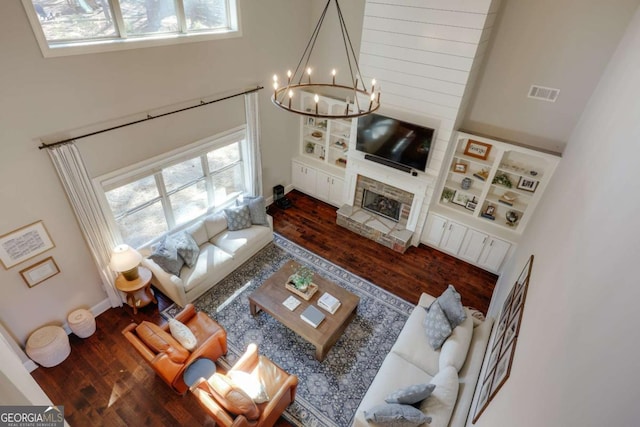 living area with visible vents, a fireplace with raised hearth, a towering ceiling, dark wood-style floors, and an inviting chandelier