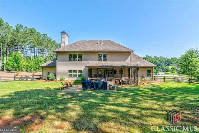 rear view of property featuring a patio area, a fenced backyard, a chimney, and a yard