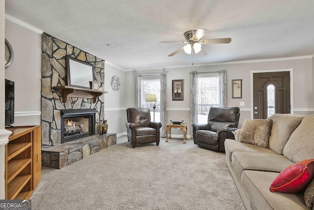 living room with a textured ceiling, a stone fireplace, carpet flooring, a ceiling fan, and crown molding