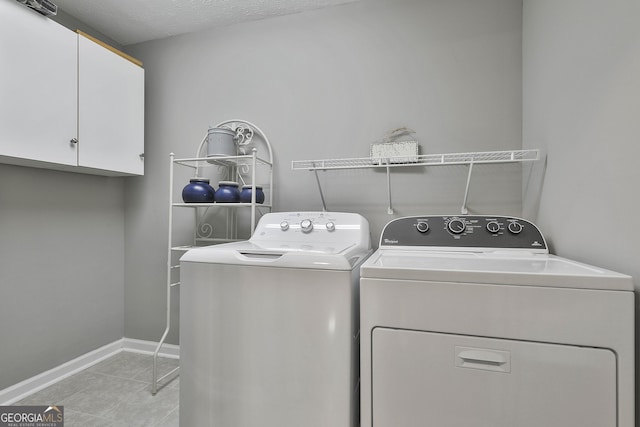 laundry room featuring light tile patterned floors, cabinet space, a textured ceiling, washer and dryer, and baseboards