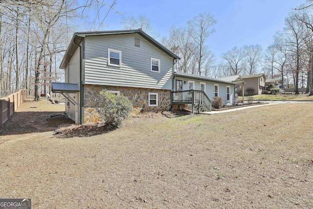 back of house featuring stone siding, fence, and a wooden deck