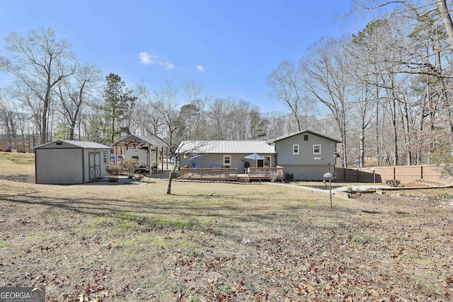 back of house featuring a deck, an outdoor structure, fence, a lawn, and a shed