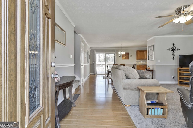 living area featuring a textured ceiling, ceiling fan with notable chandelier, baseboards, light wood-style floors, and crown molding