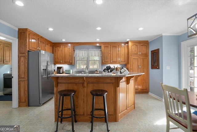 kitchen featuring stainless steel fridge, brown cabinets, plenty of natural light, and baseboards