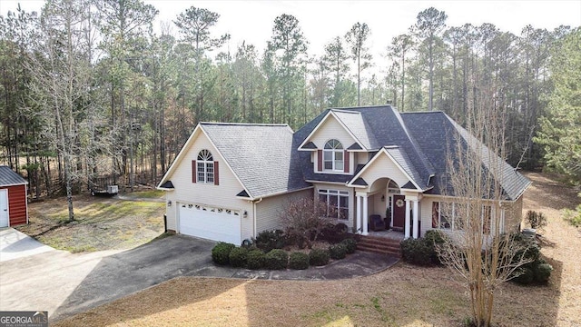 traditional-style house with driveway, an attached garage, and a wooded view