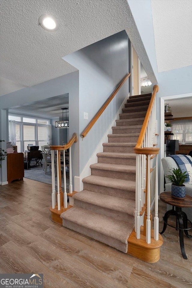 stairway with wood finished floors, an inviting chandelier, and a textured ceiling