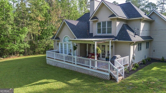 rear view of property with a chimney, roof with shingles, french doors, and a lawn