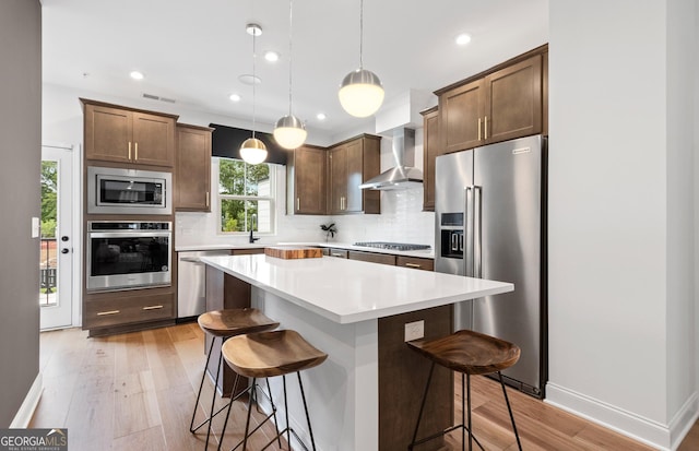 kitchen featuring stainless steel appliances, wall chimney exhaust hood, tasteful backsplash, a breakfast bar area, and light wood-style flooring