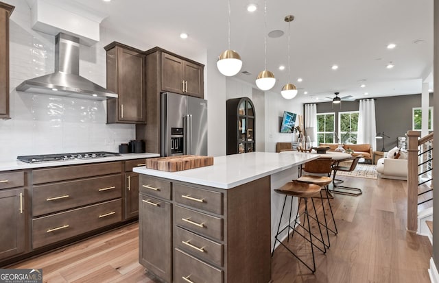 kitchen with wall chimney exhaust hood, appliances with stainless steel finishes, a kitchen breakfast bar, light wood finished floors, and arched walkways