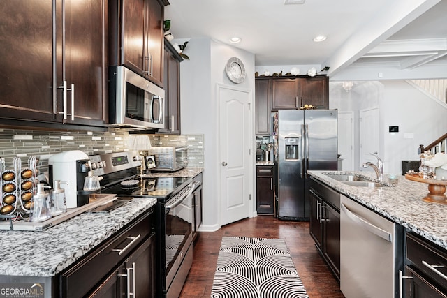 kitchen with dark wood-style floors, appliances with stainless steel finishes, dark brown cabinetry, a sink, and light stone countertops