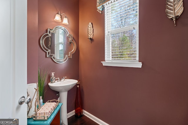 half bath featuring a sink, baseboards, and wood finished floors