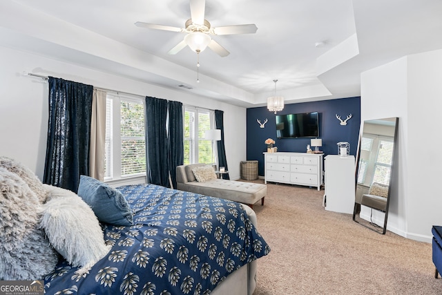 carpeted bedroom with ceiling fan with notable chandelier, a raised ceiling, visible vents, and baseboards