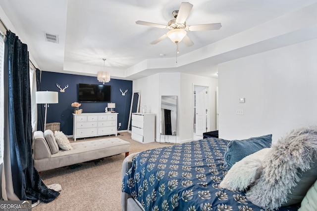 carpeted bedroom featuring a tray ceiling, visible vents, baseboards, and ceiling fan with notable chandelier