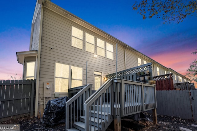 back of property at dusk featuring stairs, a wooden deck, and fence