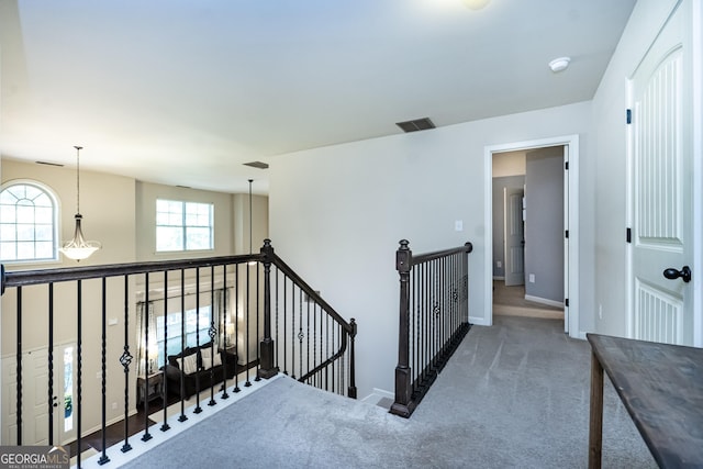 hall with baseboards, visible vents, dark colored carpet, and an upstairs landing