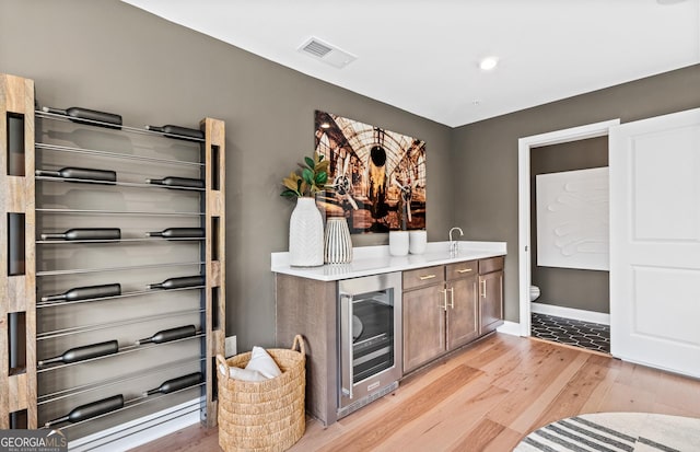 bar with wine cooler, visible vents, light wood-style flooring, and baseboards