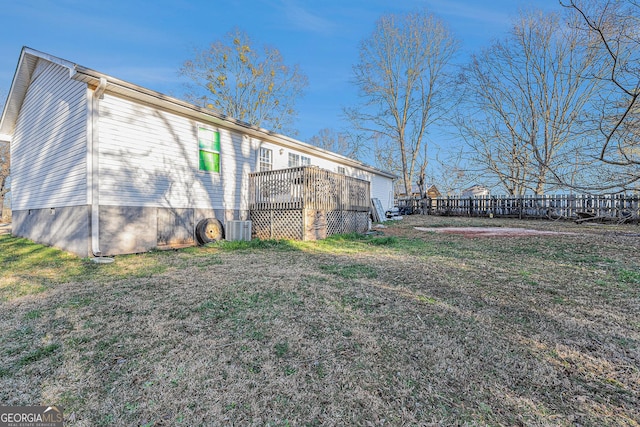 view of side of property with a lawn, a wooden deck, and fence