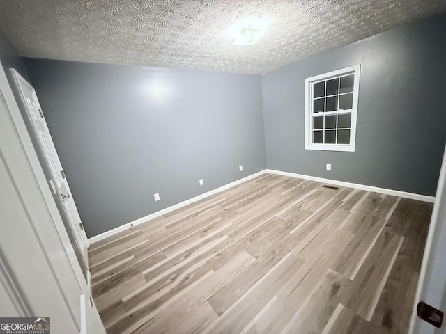 empty room featuring light wood finished floors, visible vents, baseboards, and a textured ceiling