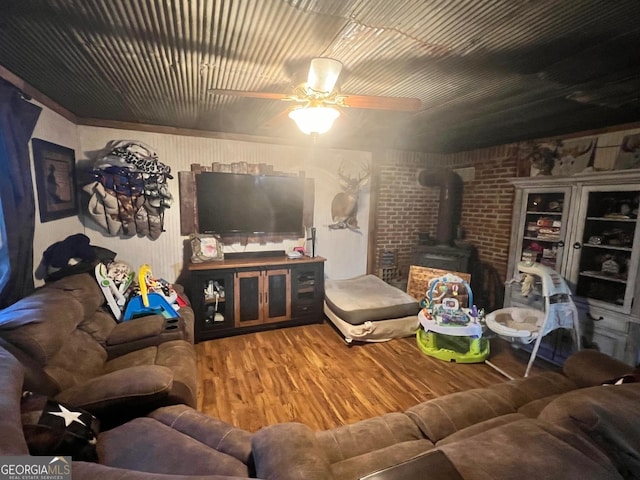 living area with a ceiling fan, a wood stove, brick wall, and wood finished floors