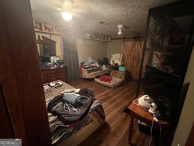 bedroom with a barn door, a textured ceiling, and wood finished floors