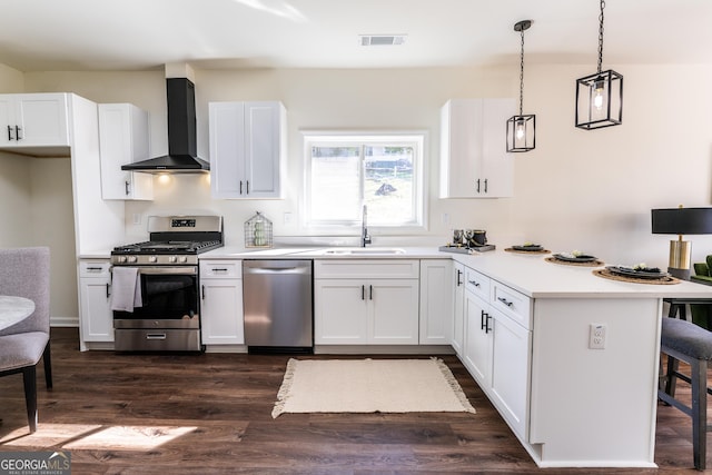 kitchen featuring a sink, white cabinets, appliances with stainless steel finishes, wall chimney exhaust hood, and decorative light fixtures