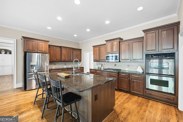 kitchen featuring stainless steel appliances, crown molding, a sink, and an island with sink