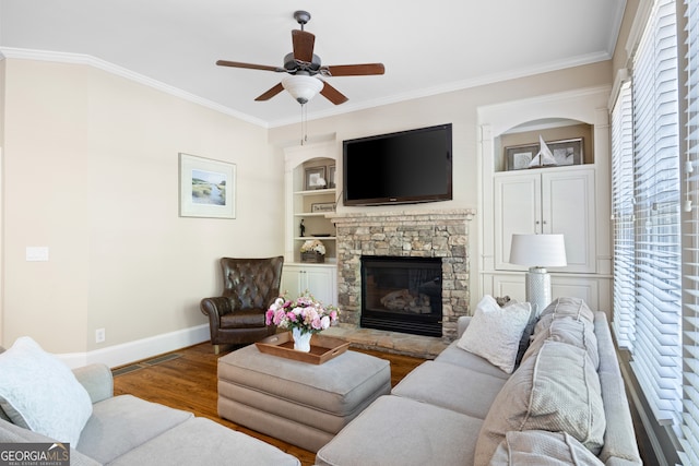 living room featuring a stone fireplace, ornamental molding, wood finished floors, and baseboards