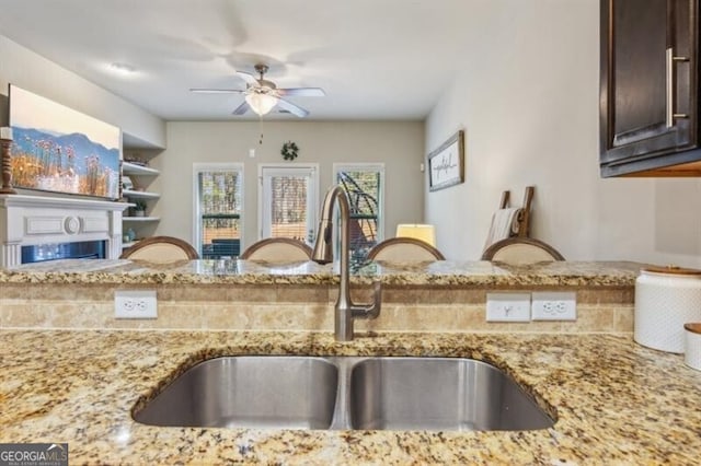 7420 Glisten Ave, Sandy Springs, GA 30328 - kitchen featuring ceiling fan, light stone counters, a fireplace, a sink, and dark brown cabinets