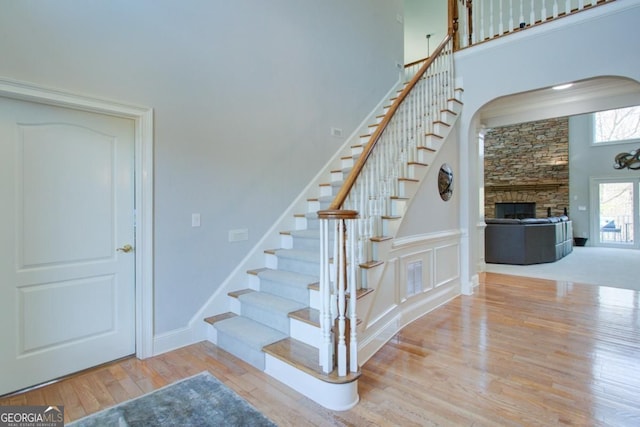 8910 Champion Ct, Ball Ground, GA 30107 - staircase featuring a stone fireplace, wood finished floors, arched walkways, a high ceiling, and baseboards