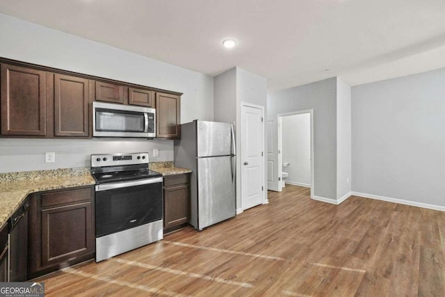 kitchen with stainless steel appliances, dark brown cabinets, light wood-type flooring, and light stone countertops