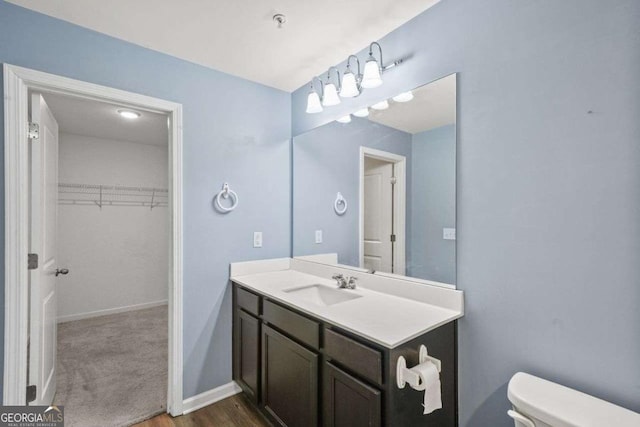 bathroom featuring vanity, a walk in closet, toilet, and baseboards