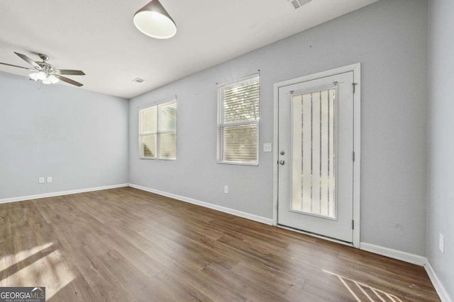 spare room with a ceiling fan, visible vents, baseboards, and wood finished floors