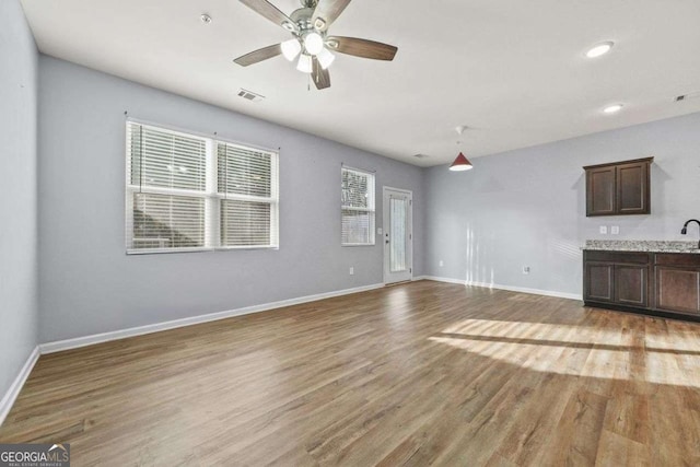 unfurnished living room with light wood-style flooring, a ceiling fan, visible vents, and baseboards