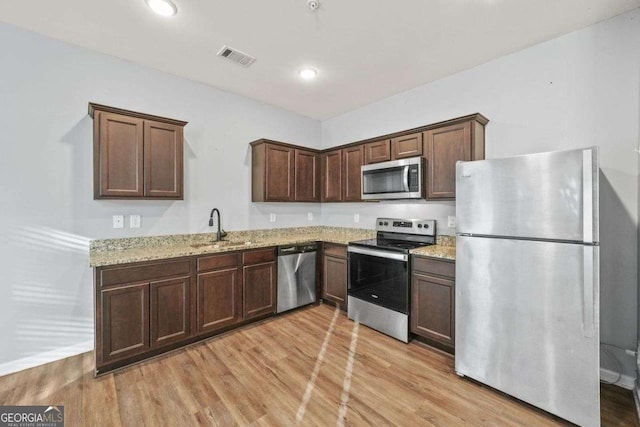 kitchen with stainless steel appliances, recessed lighting, light wood-style flooring, a sink, and light stone countertops