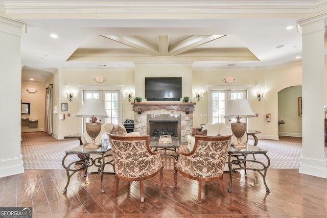 living area with arched walkways, ornamental molding, a stone fireplace, wood finished floors, and baseboards