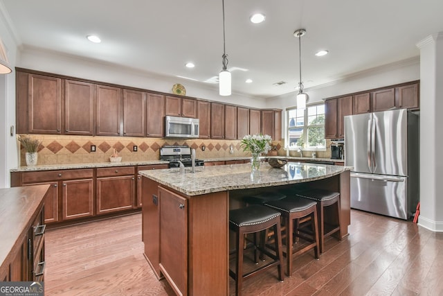 kitchen with a center island with sink, wood finished floors, decorative light fixtures, stainless steel appliances, and crown molding