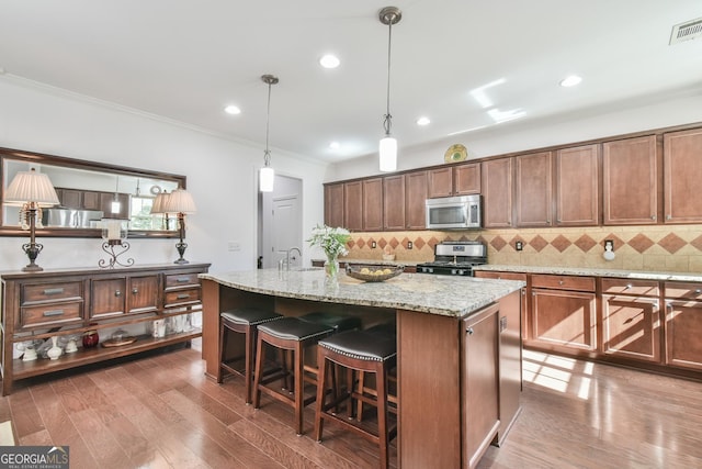 kitchen with a kitchen island with sink, appliances with stainless steel finishes, dark wood finished floors, and light stone counters