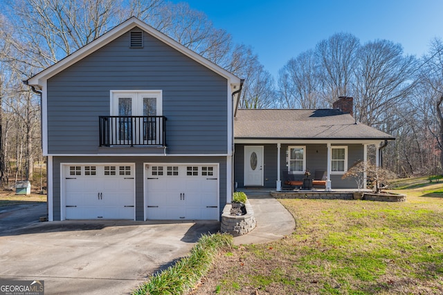 split level home with a porch, an attached garage, concrete driveway, a chimney, and a front yard