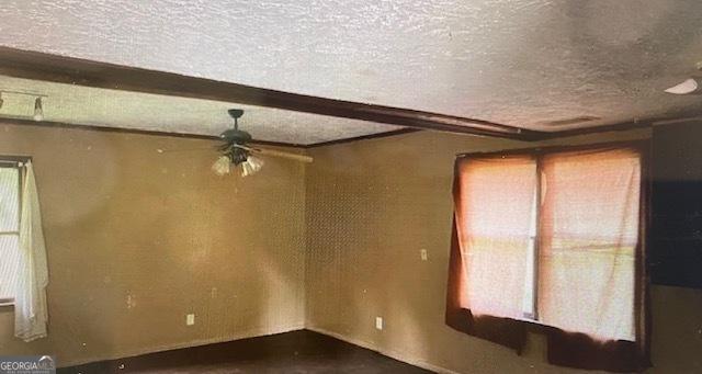 unfurnished room featuring a ceiling fan, beamed ceiling, and a textured ceiling