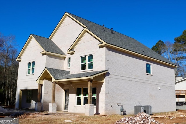 exterior space featuring covered porch, roof with shingles, central AC, and brick siding