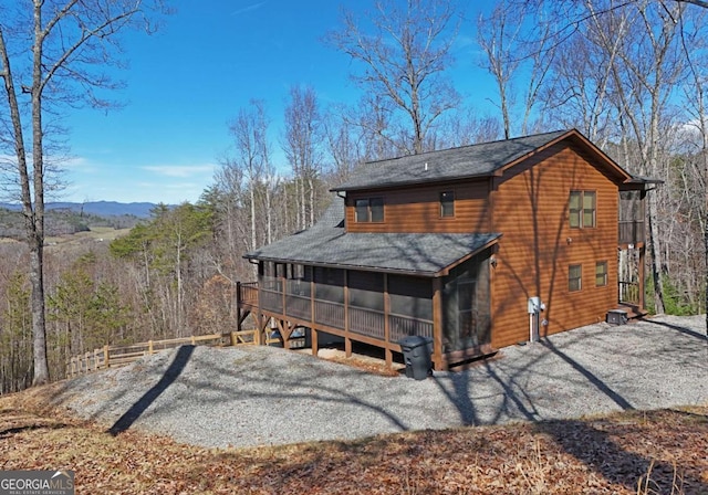 rear view of house with gravel driveway, a sunroom, and a shingled roof