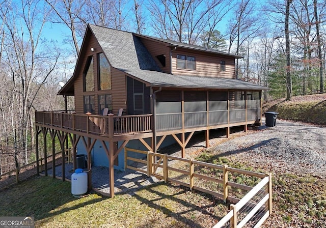 view of front of home featuring gravel driveway, a shingled roof, central AC unit, a sunroom, and faux log siding