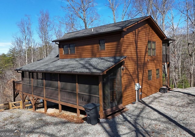 exterior space featuring a shingled roof, a sunroom, log veneer siding, and driveway