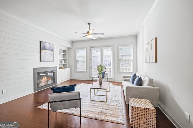 living area with built in shelves, ornamental molding, a glass covered fireplace, wood finished floors, and baseboards