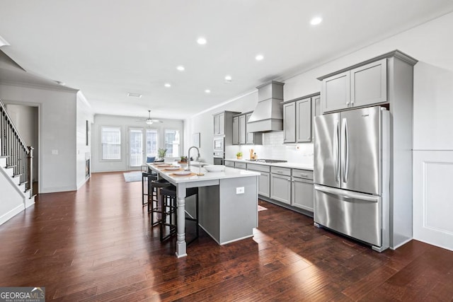 kitchen with a breakfast bar area, gray cabinetry, stainless steel appliances, custom exhaust hood, and an island with sink